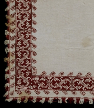 An example of 18th century Cyprian red work embroidery, possibly from Lefkara. The image shows the corner of a bed cover. It is made from linen that is embroidered with dark red silk using long-armed cross stitch, italian cross stitch, double running stitch and satin stitch.