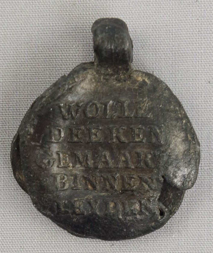 Lead, cloth seal, 18th century, with the text: WOLLE DEEKEN GEMAAKT BINNEN LEYDEN; LEYDEN HOLLAND ('woollen blanket made inside Leiden; Leiden Holland'). TRC 2016.0096).