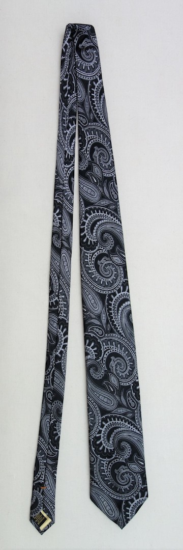 Man's tie in black with a design of stylised Paisley motifs (buteh) (TRC 2020.0395). The tie has a label that states: "DONALD J. TRUMP SIGNATURE COLLECTION", and woven into the lining is the Trump coat-of-arms. The tie also has a label stating: "Hand made in China".