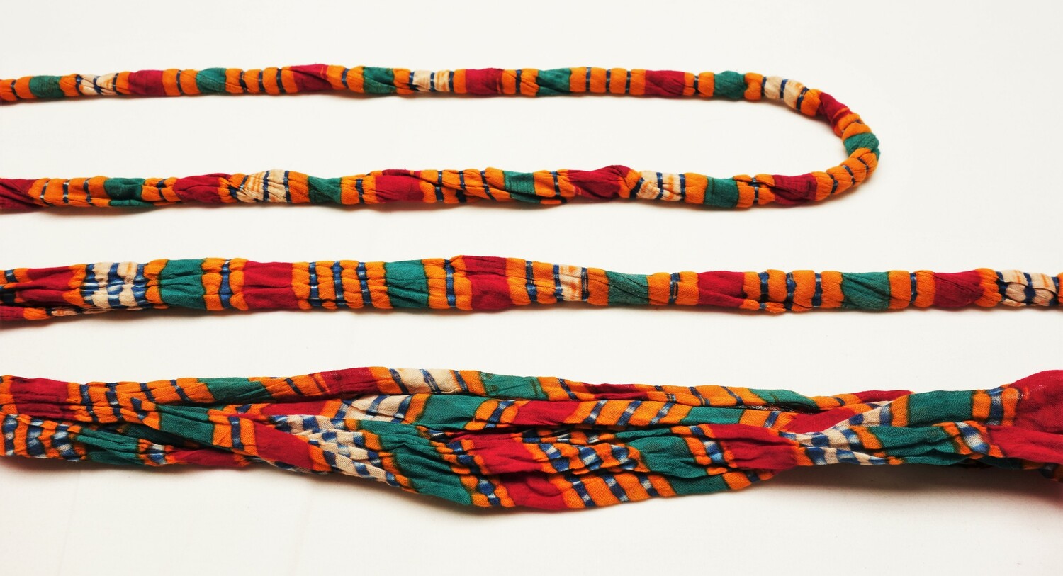 Long roll of leheria cloth that has been tied at regular intervals prior to dyeing in order to create diagonal stripes in various colours. Udaipur, Rajasthan, India (TRC 2022.2121).
