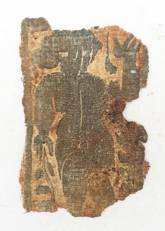 Fragment of cloth with a stylised human figure in dark purple wool on an unbleached linen ground. Hand spun and woven (dovetail tapestry, weft-faced). Coptic, mid-first millennium. Dool family donation (TRC 2023.0070).