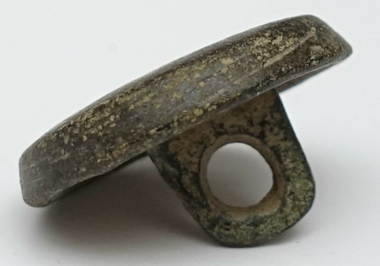 A metal button with a smooth front, curved at the edges, and an off-centre key shank. The Netherlands, 20th century (TRC 2024.2589).