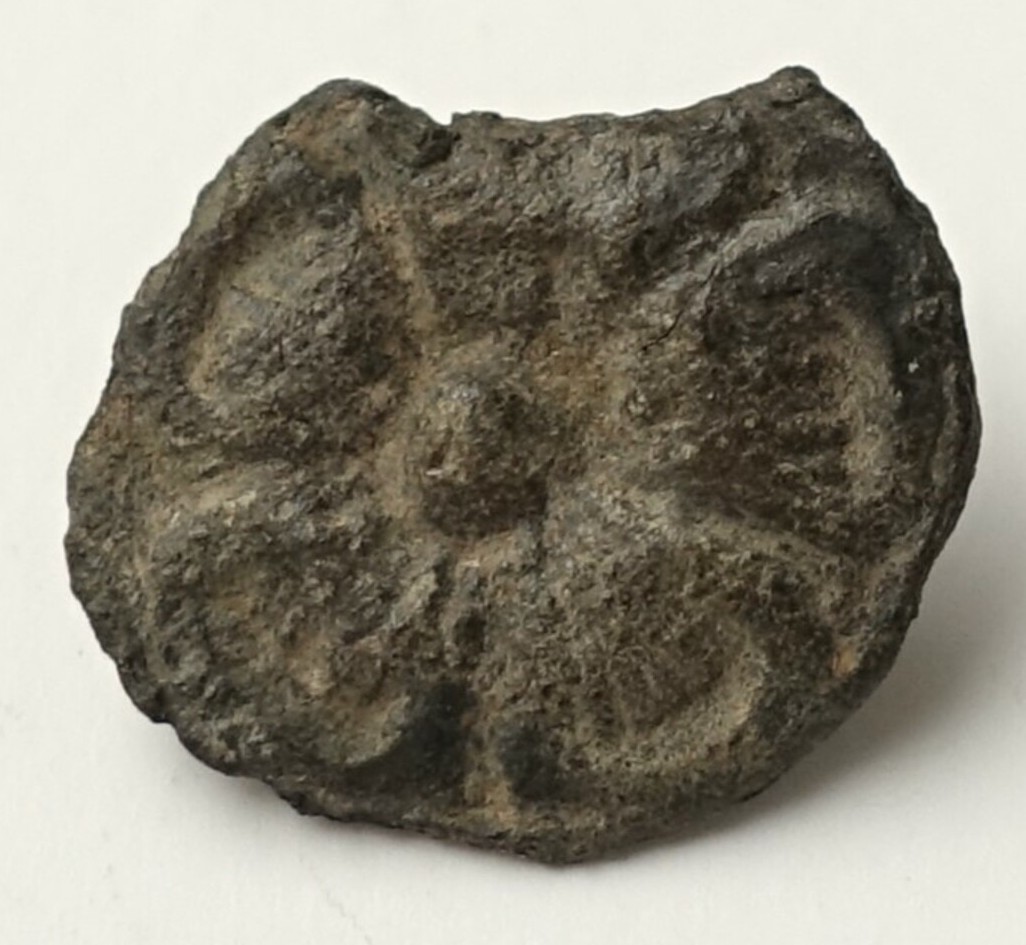Metal button with a five-petalled flower and a key shank with a tiny hole. Part of the button has broken off. Medieval. TRC 2024.2625.